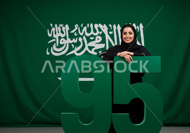 احياء الذكرى 95 لتأسيس المملكة العربية السعودية، راية التوحيد وشعار الوطن، الاحتفال بالمناسبات والأعياد الوطنية، يوم العلم 11 مارس، اليوم الوطني السعودي 23 سبتمبر، إمرأة عربية خليجية سعودية مبتسمة ترتدي الحجاب والعباءة بتعابير الاعتزاز والفخر