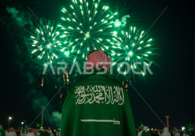 مشاهدة المفرقعات والألعاب النارية في المساء، صورة من الخلف لرجل عربي خليجي سعودي يرتدي الشماغ يضع علم المملكة العربية السعودية على كتفيه، الاحتفال بالمناسبات والأعياد الوطنية، يوم العلم 11 مارس، اليوم الوطني السعودي 23 سبتمبر، احياء الذكرى 95  للسعودية