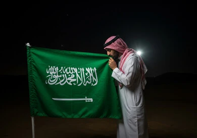 Saudi National Day, September 23, the banner of unification and the emblem of the nation, a close-up side view of a Saudi Arabian Gulf man wearing a traditional shemagh and thobe kissing the flag with gestures of pride and honor, celebrating national occasions and holidays, Flag Day, March 11