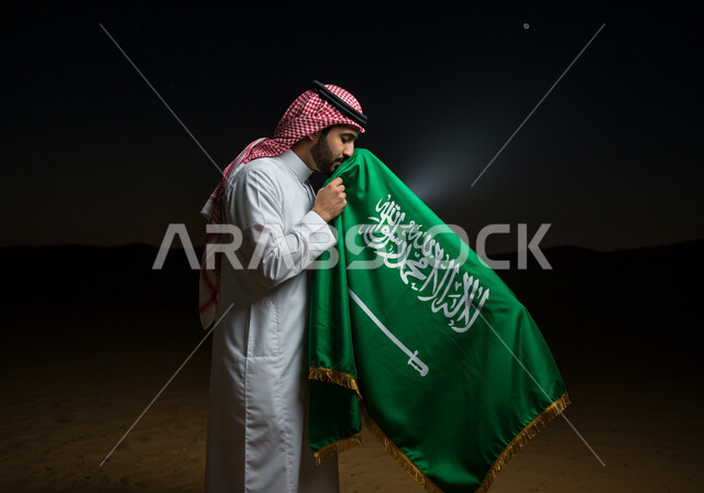 اليوم الوطني السعودي 23 سبتمبر، راية التوحيد وشعار الوطن، صورة مقربة من الجانب لرجل عربي خليجي سعودي يرتدي الشماغ والثوب التقليدي يقبل العلم بايماءات الفخر والاعتزاز، الاحتفال بالمناسبات والأعياد الوطنية، يوم العلم 11 مارس