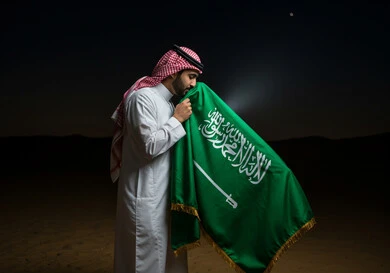 Saudi National Day, September 23, the banner of unification and the emblem of the nation, a close-up side view of a Saudi Arabian Gulf man wearing a traditional shemagh and thobe kissing the flag with gestures of pride and honor, celebrating national occasions and holidays, Flag Day, March 11