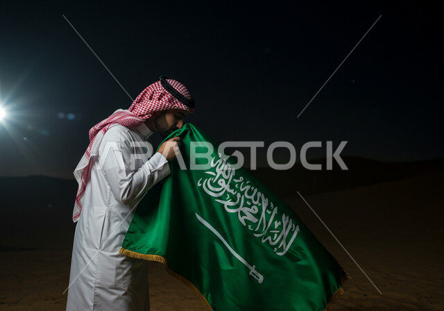 اليوم الوطني السعودي 23 سبتمبر، راية التوحيد وشعار الوطن، صورة مقربة من الجانب لرجل عربي خليجي سعودي يرتدي الشماغ والثوب التقليدي يقبل العلم بايماءات الفخر والاعتزاز، الاحتفال بالمناسبات والأعياد الوطنية، يوم العلم 11 مارس