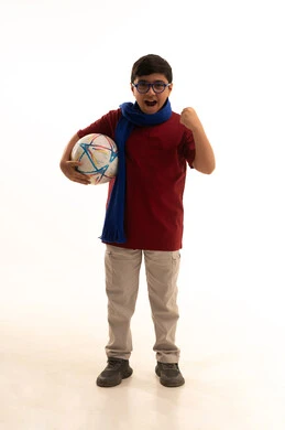 The enthusiasm for competition and expressions of joy and happiness, looking at the camera with a spirit of determination for victory, cheering for the Saudi team, ready for the challenge and win, a portrait of an Arab Gulf Saudi boy wearing casual attire and a blue scarf, raising his fist and holding a ball, full-body image, white background.