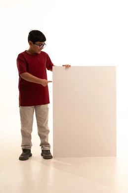 لوح إعلاني فارغ، موك أب مربع أبيض, النظر إلى الكاميرا بإيماءات السرور، استخدام لوحات تعبيرية توضيحية، بورتريه لولد عربي خليجي سعودي مبتسم يرتدي الزي الكاجوال سروال وفانيلا حمراء يقف بإستقامة ويمسك بيده لوحة مربعة بيضاء، الجسم بالطول الكامل، خلفية بيضاء