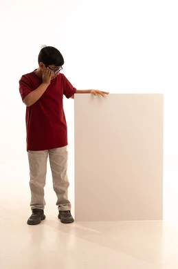 Looking with gestures of astonishment and surprise, a blank billboard, a rectangular white mock-up, using illustrative expressive boards, a portrait of a smiling Arab Gulf Saudi boy wearing casual attire, red pants and a t-shirt, standing upright and holding a white square board in his hand, full-body, white background.
