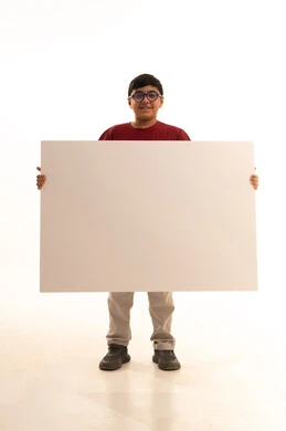 Looking at the camera with gestures of joy, a blank billboard, a white square mock-up, using illustrative expressive boards, a portrait of a smiling Arab Gulf Saudi boy wearing casual attire, red pants and a t-shirt, standing upright and holding a white square board in his hand, full body, white background.