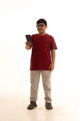 استخدام التكنولوجيا والتقنيات الحديثة، الدردشة والتواصل مع الاهل والاصدقاء عبر الجوال،  استخدام جهاز تقني حديث ومتطور، بورتريه لولد عربي خليجي سعودي يرتدي الزي الكاجوال سروال وفانيلا حمراء يمسك الهاتف المحمول,  الجسم بالطول الكامل، خلفيه بيضاء
