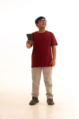 التكنولوجيا والتقنيات الحديثة، الدردشة والتواصل مع الاهل والاصدقاء عبر الجوال،  استخدام جهاز تقني حديث ومتطور، بورتريه لولد عربي خليجي سعودي يرتدي الزي الكاجوال سروال وفانيلا حمراء يمسك الهاتف المحمول,  الجسم بالطول الكامل، خلفيه بيضاء