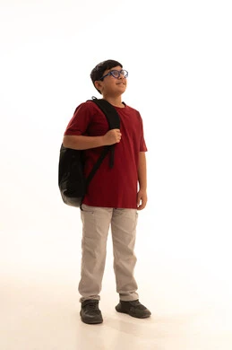 النظر لشيء ما في الأعلى، موسم العودة للمدارس في السعودية، بورتريه لطالب عربي خليجي سعودي يرتدي الزي الكاجوال سروال وفانيلا حمراء وحقيبة الظهر المدرسية يقف الحقيبة المدرسية، ولد سعودي ينظر للكاميرا بإيماءات البشاشة، الجسم بالطول الكامل، خلفية بيضاء