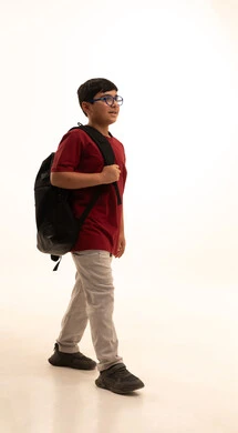 A Saudi boy looks at the camera with gestures of cheerfulness, walking and going to school every day, the back-to-school season in Saudi Arabia, a portrait of an Arab Gulf Saudi student wearing casual attire, pants and a red t-shirt, standing with a school backpack, full-body, white background.