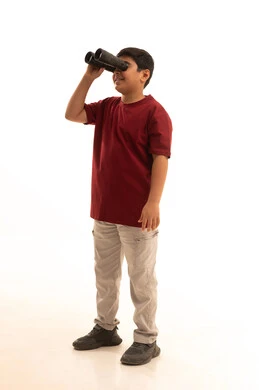 The love of exploration and adventure, seeing distant things through binoculars, pointing to something with the hand, future planning for goals and ambitions, a portrait of a smiling Arab Gulf Saudi boy wearing casual attire holding binoculars in his hand, full body, white background.