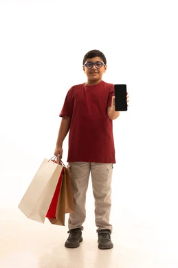 عرض شاشة سوداء فارغة عبر الهاتف المحمول، مفهوم التسوق عن بعد, عمليات الشراء الالكتروني عبر الانترنت, بورتريه لولد عربي خليجي سعودي يرتدي الزي الكاجوال يمسك بيده أكياس ورقية ملونة, التبضع والاستفادة من العروض والتخفيضات, الجسم بالطول الكامل, خلفية بيضاء