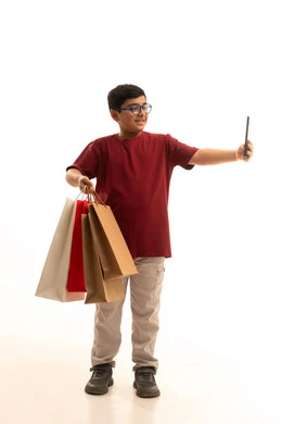 توثيق اللحظات الجميلة التقاط صورة سيلفي، مفهوم التسوق عن بعد, عمليات الشراء الالكتروني عبر الانترنت, بورتريه لولد عربي خليجي سعودي يرتدي الزي الكاجوال يمسك بيده أكياس ورقية ملونة, التبضع والاستفادة من العروض والتخفيضات, الجسم بالطول الكامل, خلفية بيضاء