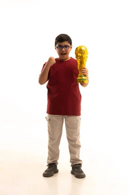 Gestures of happiness and joy, the concept of profit and victory, a portrait of an Arab Gulf Saudi boy wearing casual attire, red pants and a t-shirt, holding the golden World Cup for football in his hand, physical activity to maintain body health and fitness, full-length body, white background. Gestures of happiness and joy, the concept of profit and victory, a portrait of an Arab Gulf Saudi boy wearing casual attire, red pants and a t-shirt, holding the golden World Cup for football in his hand, physical activity to maintain body health and fitness, full-length body, white background.