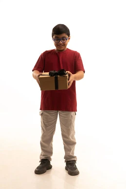 تقديم الهدايا في المناسبة السعيدة,التعبير عن المحبة والتقدير,  الاحتفال بعيد الميلاد, بورتريه لولد عربي خليجي سعودي يرتدي الزي الكاجوال  يمسك بيديه علبة هدية ينظر إلى الهدية  بإيماءات السرور والسعادة، الجسم بالطول الكامل، خلفية بيضاء