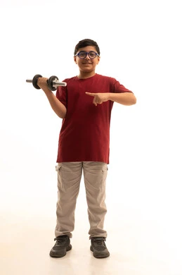 A hobby of practicing sports since childhood, looking at the camera with gestures of joy, lifting heavy weights, a portrait of an Arab Gulf Saudi boy wearing casual attire holding heavy iron weights (dumbbells) in his hand, recreational sports activities for children, full-body shot, white background.