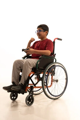 ايماءات الفوز والانتصار، تجربة مثيرة في الأجهزة الحديثة الالكترونية، نشاطات ترفيهية لذوي الهمم، التفاعل والاندماج مع ألعاب البلايستيشن, بورتريه لولد عربي خليجي سعودي مقعد يرتدي الزي الكاجوال والنظارة الطبية يجلس على كرسي متحرك يحمل بيده عصا التحكم، خلفية بيضاء