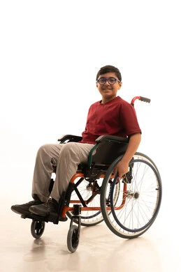 Elegance and attention to appearance, looking at the camera with gestures of joy and happiness, a portrait of an Arab Gulf Saudi boy with special needs wearing casual attire and glasses sitting in a wheelchair, with a white background.