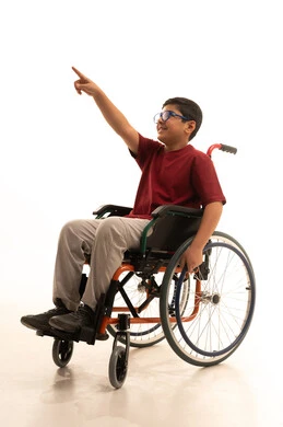 Pointing with the index finger at something, a portrait of an Arab Gulf Saudi boy with special needs wearing casual attire and glasses, sitting in a wheelchair looking at something, with a white background.