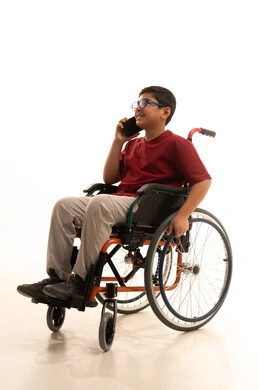 استخدام الأجهزة التقنية والتكنولوجيا الحديثة، تصفح مواقع التواصل الاجتماعي، بورتريه لولد عربي خليجي سعودي من ذوي الاحتياجات الخاصة يرتدي الزي الكاجوال والنظارة الطبية يجلس على كرسي متحرك يقوم بإجراء مكالمة هاتفية باستخدام الهاتف المحمول، خلفية بيضاء