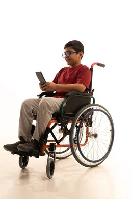 استخدام الأجهزة التقنية والتكنولوجيا الحديثة، تصفح مواقع التواصل الاجتماعي، بورتريه لولد عربي خليجي سعودي من ذوي الاحتياجات الخاصة يرتدي الزي الكاجوال والنظارة الطبية يجلس على كرسي متحرك يمسك الهاتف المحمول بيده بإيماءات السرور، خلفية بيضاء