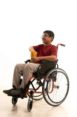 انشطة ترفيهية منزلية، مشاهدة الافلام والعروض المسرحية، بورتريه لولد عربي خليجي سعودي مقعد يرتدي الزي الكاجوال والنظارة الطبية يجلس على كرسي متحرك يحمل بيده دلو الفشار، تناول الوجبات الخفيفة والسناك، خلفية بيضاء