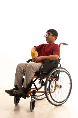 انشطة ترفيهية منزلية، مشاهدة الافلام والعروض المسرحية، بورتريه لولد عربي خليجي سعودي مقعد يرتدي الزي الكاجوال والنظارة الطبية يجلس على كرسي متحرك يحمل بيده دلو الفشار، تناول الوجبات الخفيفة والسناك، خلفية بيضاء