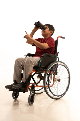 The love of exploration and adventure, future planning for goals and ambitions, a forward-looking vision for people with determination, a portrait of a young Arab Gulf Saudi boy in a wheelchair wearing casual attire and glasses, sitting in a wheelchair, holding binoculars in his hand and pointing with his index finger at something, with a white background.