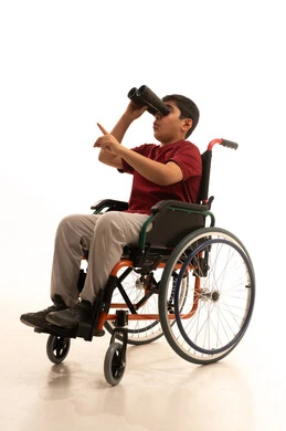 حب الاستكشاف والمغامرة ،التخطيط المستقبلي للأهداف والطموحات ، رؤية مستقبلية عند ذوي الهمم، بورتريه لولد عربي خليجي سعودي مقعد يرتدي الزي الكاجوال والنظارات الطبية يجلس على كرسي متحرك و يحمل بيده المنظار ثنائي العينين ويشير بإصبع السبابة إلى شيء ما، خلفية بيضاء.