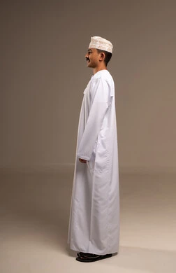 Facial expressions and body language, representing authentic Arab masculinity, standing with arms crossed with gestures of joy and happiness, a side portrait of a Gulf Arab Omani man wearing a dishdasha and kumma, standing and smiling, the concept of dignity and elegance, maintaining traditional attire, full-length body, beige background.
