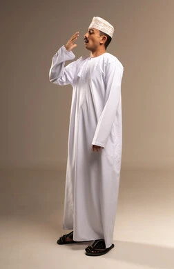 الشعور بالنعاس والتثائب، تمثيل الرجولة العربية الأصيلة،  إيمات التعب والالم،، بورتريه  لرجل عربي خليجي عماني يرتدي الدشداشة والكمة يقف ، مفهوم الهيبة والاناقة، المحافظة على لبس اللباس التقليدي، الجسم بالطول الكامل، خلفية بيج