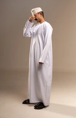 التعب والشعور بالنعاس والتثائب، تمثيل الرجولة العربية الأصيلة، إيمات التعب والالم،، بورتريه  لرجل عربي خليجي عماني يرتدي الدشداشة والكمة يقف ، مفهوم الهيبة والاناقة، المحافظة على لبس اللباس التقليدي، الجسم بالطول الكامل، خلفية بيج