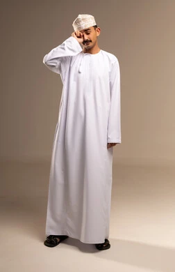 ألم في العين والرأس، تمثيل الرجولة العربية الأصيلة،  إيمات التعب والالم،، بورتريه  لرجل عربي خليجي عماني يرتدي الدشداشة والكمة يقف ويضع يده على عينه، مفهوم الاهتمام بالاناقة والمظهر الخارجي، المحافظة على لبس اللباس التقليدي، الجسم بالطول الكامل، خلفية بيج