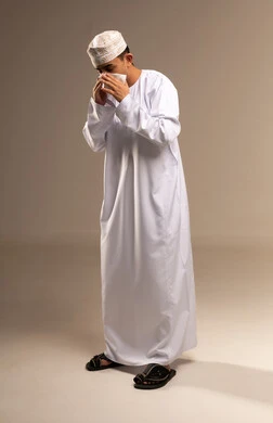 The handkerchief for cleaning the nose, sinuses, and allergies, representing Arab masculinity, expressions of fatigue and pain, a portrait of an Arab Gulf Omani man wearing a dishdasha and kumma, the concept of caring about elegance and appearance, maintaining traditional clothing, full-body, beige background.