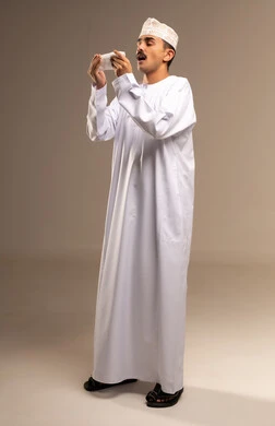 العطاس والسعال وقت المرض، الجيوب والانفية والحساسية، تمثيل الرجولة العربية،  إيمات التعب والالم، بورتريه  لرجل عربي خليجي عماني يرتدي الدشداشة والكمة، مفهوم الاهتمام بالاناقة والمظهر الخارجي، المحافظة على لبس اللباس التقليدي، الجسم بالطول الكامل، خلفية بيج
