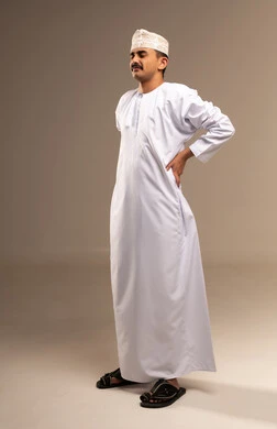 وضع اليدين على الظهر ، التعب وتحمل الالام ، الذهاب للطبيب لمعالجة الاوجاع، تمثيل الرجولة العربية،  بورتريه  لرجل عربي خليجي عماني يرتدي الدشداشة والكمة، مفهوم الاهتمام بالاناقة والمظهر الخارجي، المحافظة على لبس اللباس التقليدي، الجسم بالطول الكامل، خلفية بيج