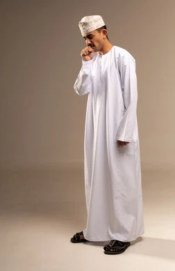 Coughing and sneezing during the flu, fatigue and enduring pain, going to the doctor to treat aches, representing Arab masculinity, a portrait of an Omani Gulf Arab man wearing a dishdasha and kumma, the concept of caring about elegance and appearance, maintaining traditional dress, full-body, beige background.