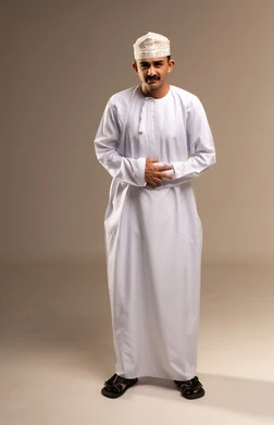 مغص في المعدة والتهاب الامعاء، التعب وتحمل الالام ، الذهاب للطبيب لمعالجة الاوجاع، تمثيل الرجولة العربية،  بورتريه  لرجل عربي خليجي عماني يرتدي الدشداشة والكمة، مفهوم الاهتمام بالاناقة والمظهر الخارجي، المحافظة على لبس اللباس التقليدي، الجسم بالطول الكامل، خلفية بيج