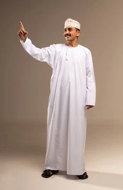 Raising the index finger upwards is an expression of the number one, a gesture for something, achieving goals and reaching the aim, the concept of elegance and masculinity, a portrait of an Arab Gulf Omani man wearing a dishdasha and a kumma standing, attention to external appearance, full-length body, beige background.