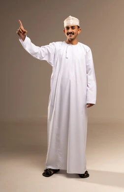 الاشارة لشيء ما، رفع السبابة للاعلى تعبير عن رقم واحد ، تحقيق الاهداف والوصول الى الغاية، مفهوم الأناقة والرجولة، بورتريه لرجل عربي خليجي عماني يرتدي الدشداشة والكمة يقف، الاهتمام بالمظهر الخارجي، الجسم بالطول الكامل، خلفية بيج