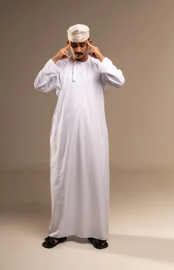 التوتر والضغط العالي، وضع الاصبعين السبابة على الرأس ، الم في مقدمة الرأس بسبب التعب، تعابير التعب والارهاق، مفهوم الأناقة والرجولة، بورتريه لرجل عربي خليجي عماني يرتدي الدشداشة والكمة يقف، الاهتمام بالمظهر الخارجي، الجسم بالطول الكامل، خلفية بيج