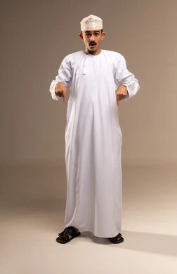 استخدام اصبع السابة في الحركات والتعبيرات، الاشارة الى القدمين، تعابير الدهشة والتفاجأ، تحديد موقع او هدف معين، مفهوم الأناقة والرجولة، بورتريه لرجل عربي خليجي عماني يرتدي الدشداشة والكمة يقف، الاهتمام بالمظهر الخارجي، الجسم بالطول الكامل، خلفية بيج
