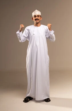Raising his fists up in gestures of victory and triumph, a portrait of a smiling Arab Gulf Omani man wearing a dishdasha and kumma, looking at the camera with expressions of joy and pride, the concept of caring about external appearance and elegance, accomplishing the required task, full-body, beige background.