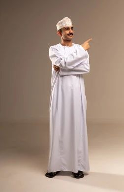 الوقوف باستقامة والنظر إلى الكاميرا بتعابير السعادة, بورتريه لرجل عربي خليجي عماني يرتدي الدشداشة والكمه حركات اليدين والإشارة بأصابع السبابة إلى اتجاه ما بإيماءات الثقة بالنفس, مفهوم الأناقة والرجولة والاهتمام بالمظهر الخارجي, خلفية بيج