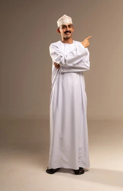 حركات اليدين والإشارة بأصابع السبابة إلى اتجاه ما بإيماءات الثقة بالنفس, الوقوف باستقامة والنظر إلى الكاميرا بتعابير السعادة, بورتريه لرجل عربي خليجي عماني يرتدي الدشداشة والكمه  مفهوم الأناقة والرجولة والاهتمام بالمظهر الخارجي, خلفية بيج