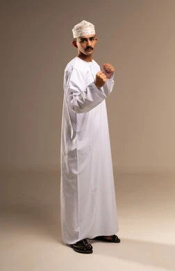 احتراف رياضة الملاكمة، إغلاق اليدين والاستعداد للهجوم والمواجهة، محاولة الدفاع عن النفس، مفهوم القوة والرجولة، بورتريه لرجل عربي خليجي عماني يرتدي الدشداشة والكمه ينظر للكاميرا بإيماءات الجدية والغضب، الجسم بالطول الكامل، خلفية بيج