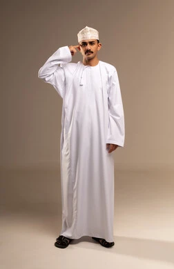 الإشارة إلى الرأس بإيماءات الثقة بالنفس، مفهوم الحكمة و الوعي، التفكير بشكل صحيح وسليم، المقدرة على حل المشكلات وإعطاء النصائح، بورتريه لرجل عربي خليجي عماني مبتسم يرتدي الدشداشة والكمه ينظر إلى الكاميرا بتعابير البشاشة، الجسم بالطول الكامل، خلفية بيج