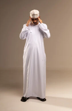 آلام الشقيقة والصداع النصفي ,إيماءات الألم والتعب والمرض, بورتريه لرجل عربي خليجي عماني يرتدي الدشداشة والكمه يضع يديه على رأسه يشعر بالدوار, الإحساس بوجع الرأس و الدوخة, الحاجة للعلاج والراحة، الجسم بالطول الكامل، خلفية بيج