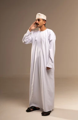 ايماءات التحذير والمناداه، بورتريه لرجل عربي خليجي عماني يرتدي الدشداشة والكمه يقوم بمناداة شخص ما بايماءات الانصات والتركيز، إيماءات وجه ويدين تدل على المناداه, النداء بصوت مرتفع,  تعابير وجه ويد تدلان على التنبيه من حدوث مصيبة ما، الجسم بالطول الكامل، خلفية بيج