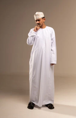 إلتهاب اللثه و تسوس الأضراس، طلب العلاج والمساعده، يعاني من مشاكل صحية في الاسنان ، بورتريه لرجل عربي خليجي عماني يرتدي الدشداشة والكمه يضع يده على خده بإيماءات تدل على الشعور بألم الأسنان، الحاجه لزيارة الطبيب، الجسم بالطول الكامل, خلفية بيج